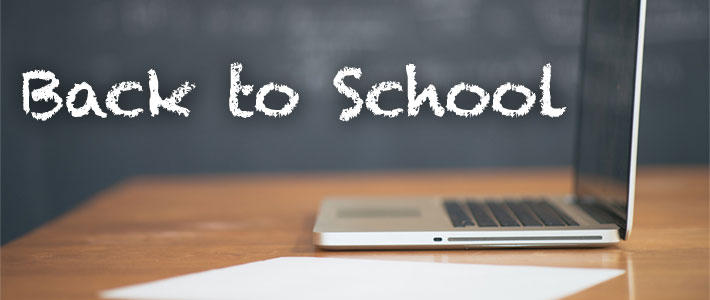 A laptop and white sheet of paper rest on a wooden desk. The text in this image reads "Back to School".